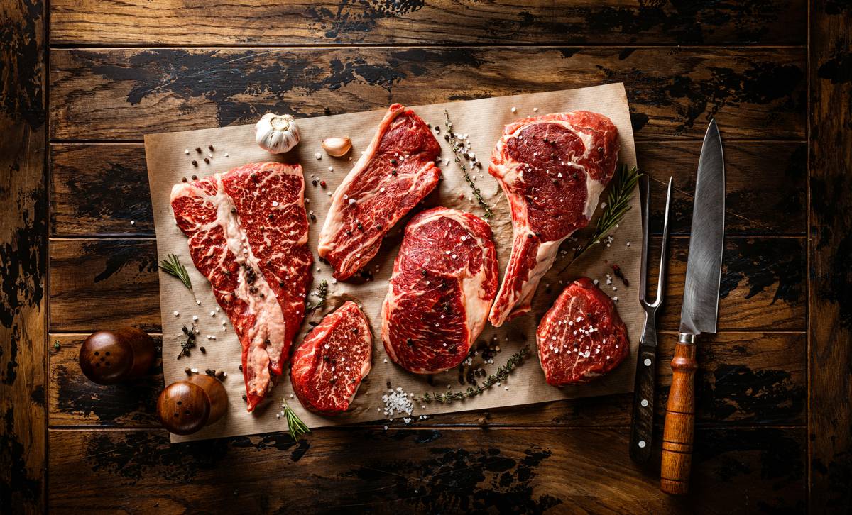 tool for tenderizing meat shown alongside raw beef cuts on a butcher block